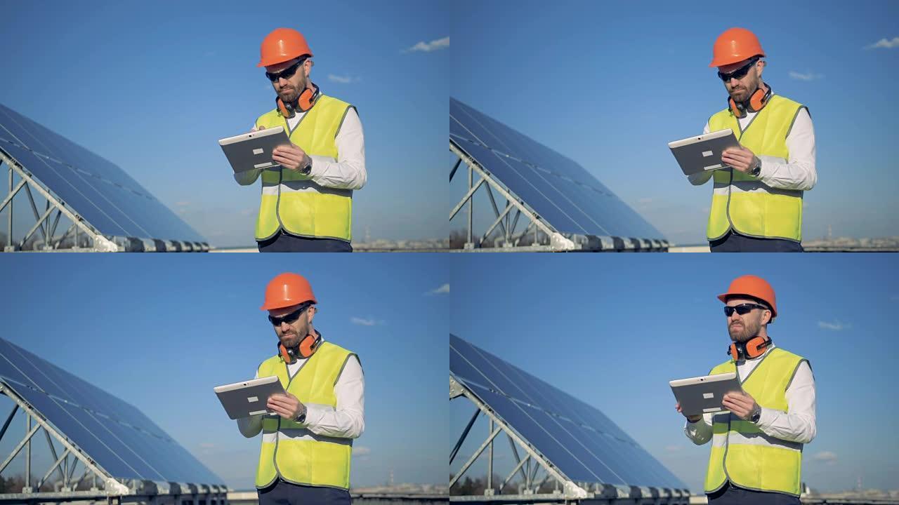 工程师站在太阳能电池板附近的屋顶上，在他的小工具上工作。4K。