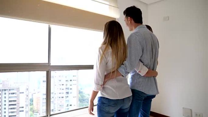 激动的夫妇看着一处新房产，房地产经纪人一边聊天一边欣赏卧室的景色