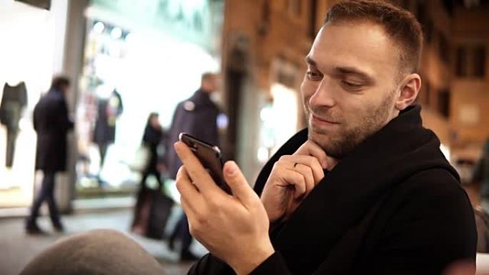 年轻英俊的男人晚上坐在咖啡馆里，在互联网上使用智能手机，独自一人度过