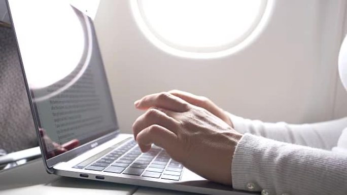 特写: 在长途飞行中，女性的手指在光滑的笔记本电脑键盘上打字。