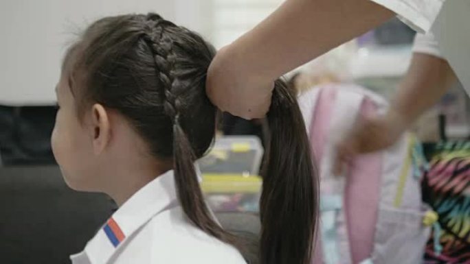 母亲上学前编织女儿的头发。