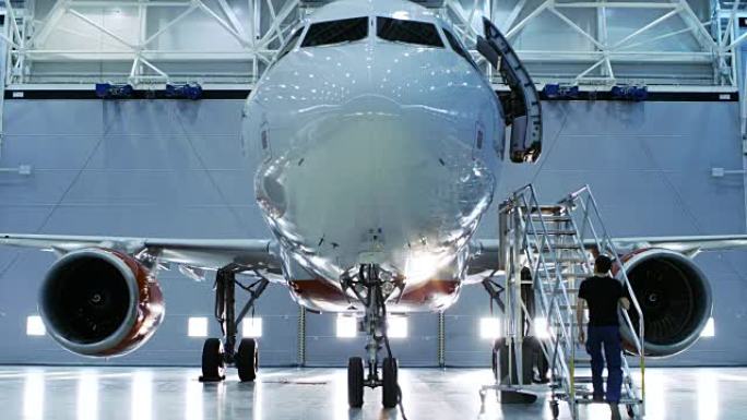 全新的飞机站在飞机维修机库中，而飞机维修工程师/技术员/机械师通过梯子/坡道进入机舱。