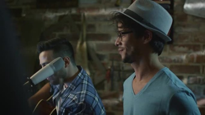 两个年轻人在车库的家庭工作室里排练一首歌时唱歌和弹吉他。