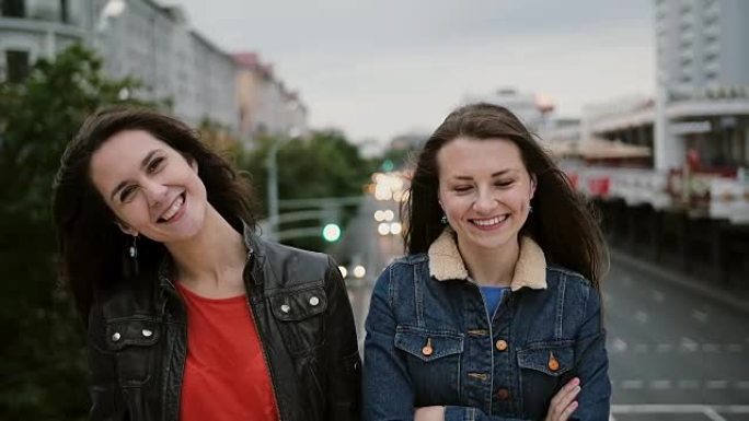 两个漂亮的女孩站在桥上，微笑着，笑着看着镜头。风吹他们长发