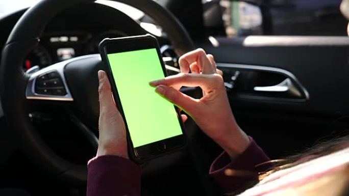 女人在汽车上使用带有绿屏的智能手机