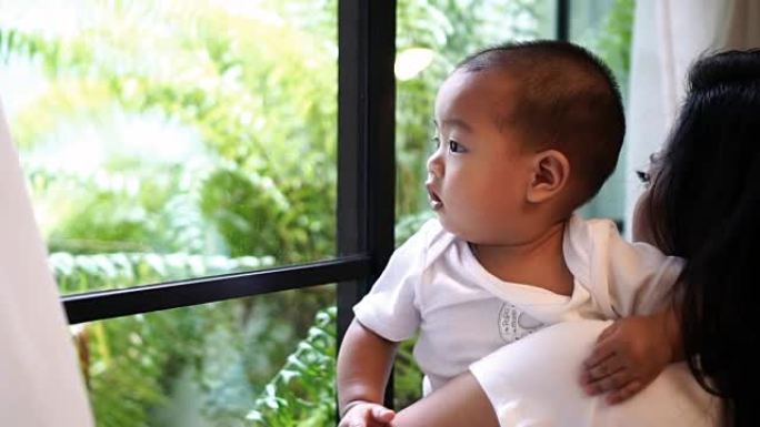 慢动作FHD剪辑亚洲男婴凝视和触摸窗户玻璃的镜头，而他的母亲在现代阁楼房子，家庭和生活方式的概念