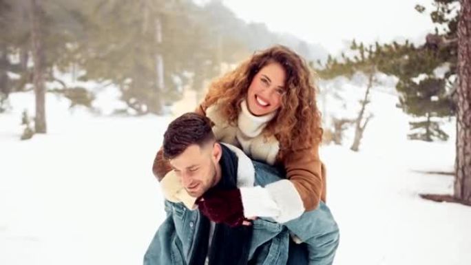 时髦的夫妇在白雪皑皑的森林里享受背负式骑行和接吻
