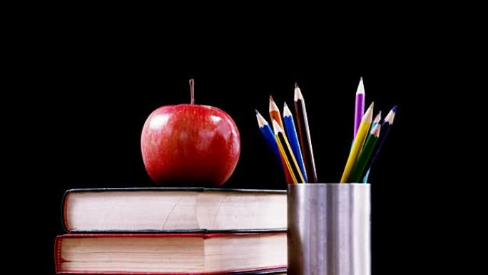 苹果在书堆上，桌上有彩色铅笔