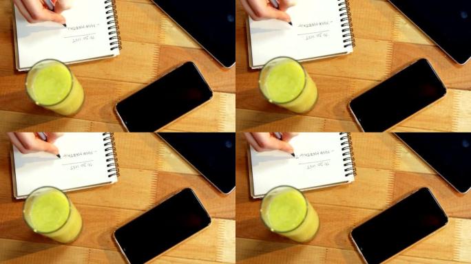 女商人的手在桌子上的笔记本上写字，桌上放着一杯果汁和手机