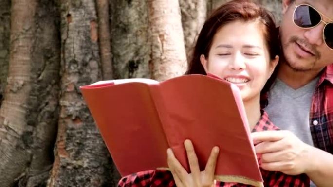 幸福的年轻迷人夫妇在公园里一起，女孩看书