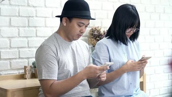 在现代共同工作空间、生活方式和休闲概念中，穿着休闲套装的亚洲夫妇使用智能手机的4k镜头场景