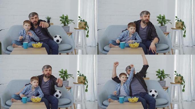 足球迷大胡子的男人和他的小孩正在家里看电视比赛，庆祝进球和吃薯片。花时间与家庭和运动概念在一起。