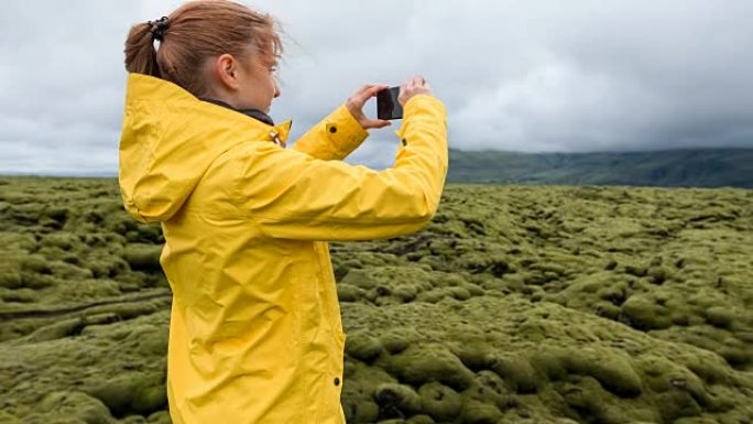 穿着黄色雨衣的女人在大风天拍摄绿色和苔藓的火山景观