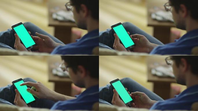 男人躺在家里的沙发上，在肖像模式下使用带有绿屏的Android手机。
