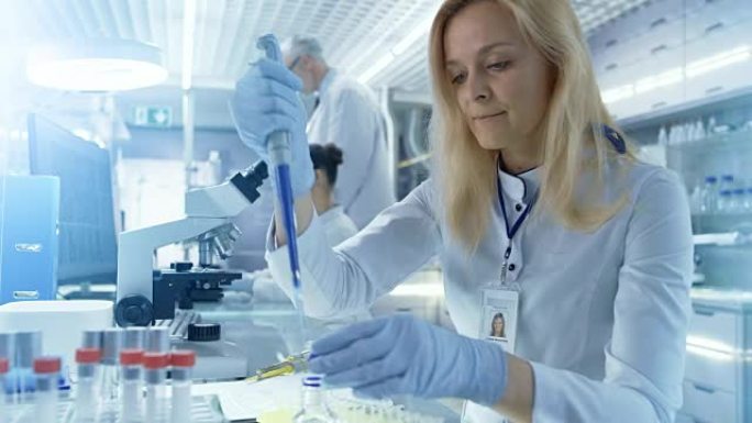 女研究科学家使用微量移液器填充试管在一个大型的现代实验室。在背景下，科学家正在工作。