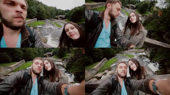 一对美丽的年轻夫妇正在瀑布上的木桥上摆姿势自拍