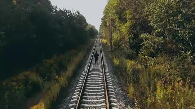 在秋季森林铁路上奔跑的人。无人机后视图。运动员在通往清晰视野的道路上。电影镜头