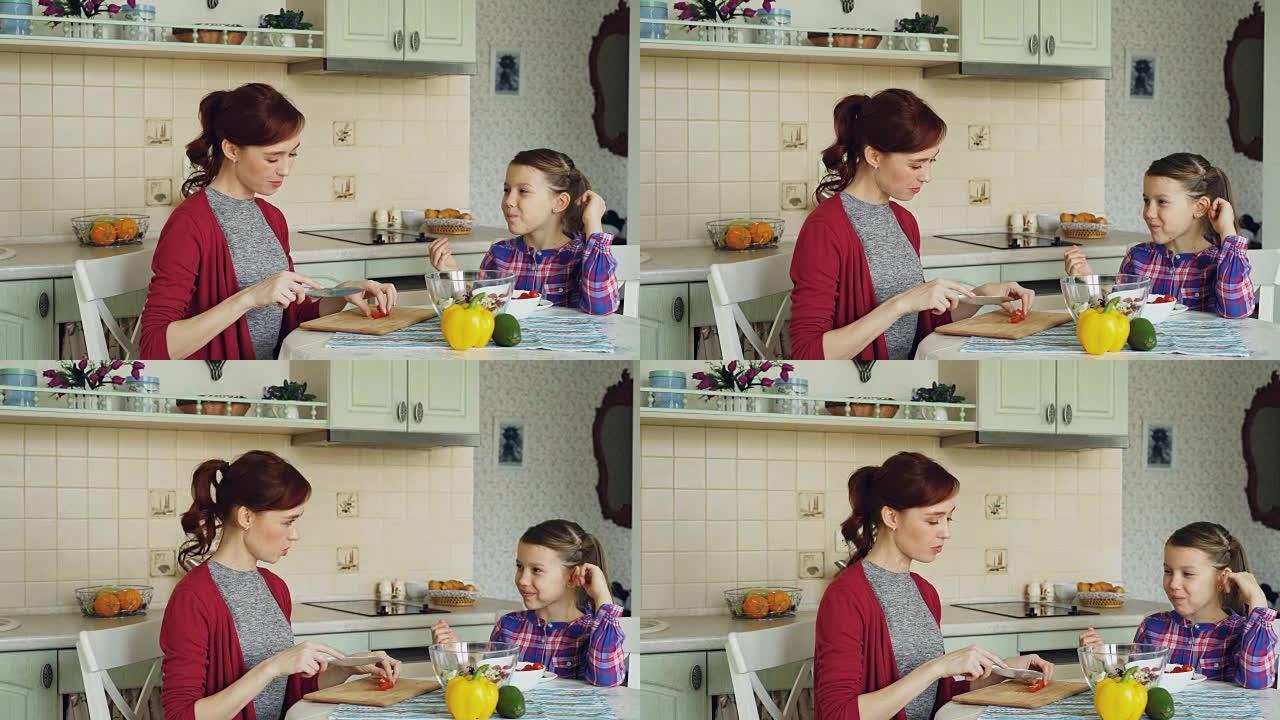 快乐的年轻母亲在家里的厨房里煮菜和开朗的女儿聊天。家庭、厨师和人的概念