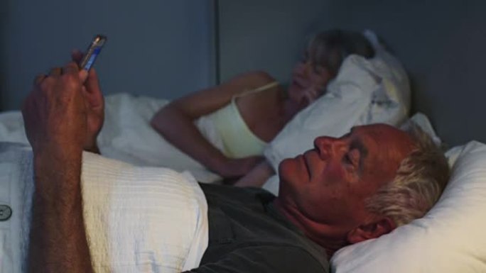晚上睡觉的老人在床上使用手机