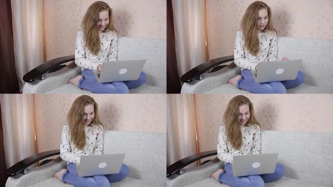 快乐美丽的女孩用笔记本电脑在沙发上放松，对着镜头微笑