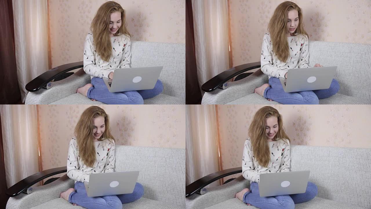 快乐美丽的女孩用笔记本电脑在沙发上放松，对着镜头微笑
