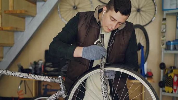 集中的年轻机械师在他的小型家庭工作室修理自行车时，正在给自行车车轮润滑，并用耳机听音乐。维护和人的概