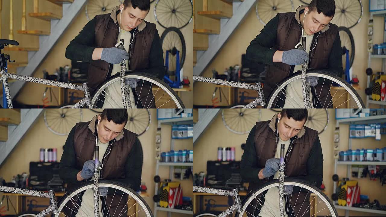 集中的年轻机械师在他的小型家庭工作室修理自行车时，正在给自行车车轮润滑，并用耳机听音乐。维护和人的概
