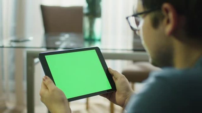 男人在家里以风景模式拿着带有绿屏的平板电脑。在4k (UHD) 的红色电影相机上拍摄。
