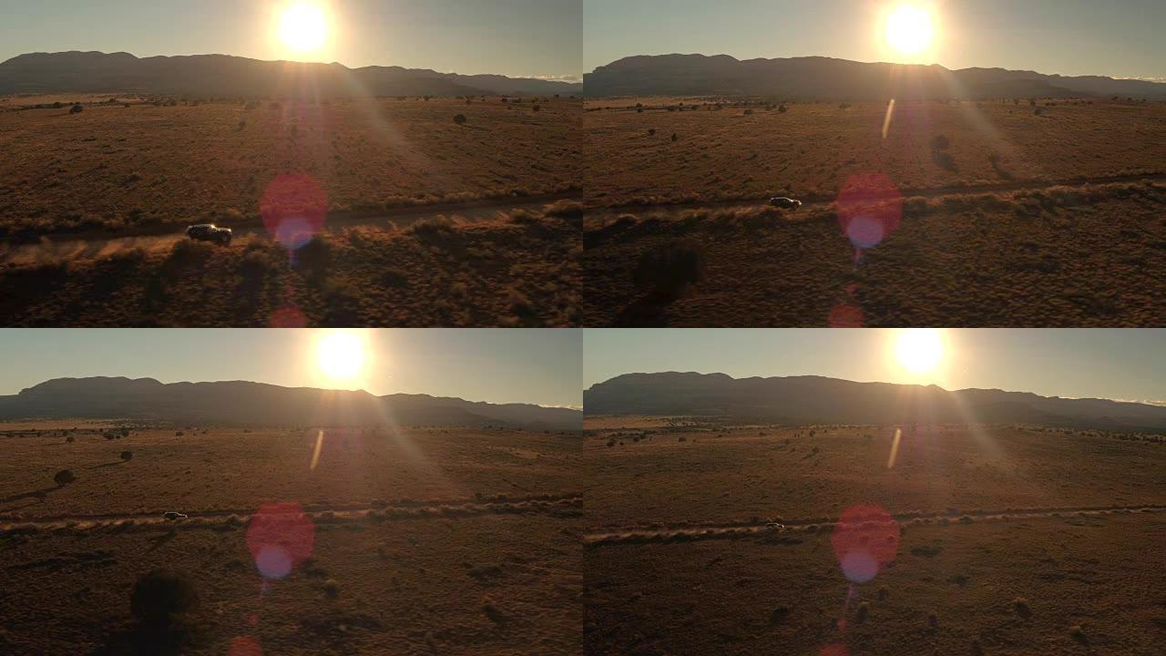 空中黑色越野车行驶在沙漠山谷尘土飞扬的道路在金色的日出