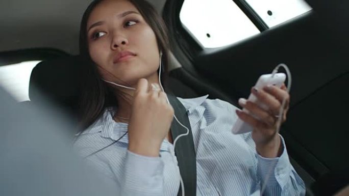 亚洲女士在汽车上的智能手机上听音乐