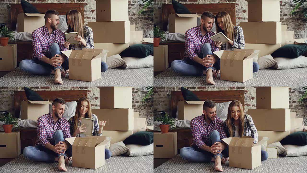 已婚夫妇坐在新房子的地板上时正在打开私人物品的包装。年轻人有说有笑，纸箱和双人床可见。