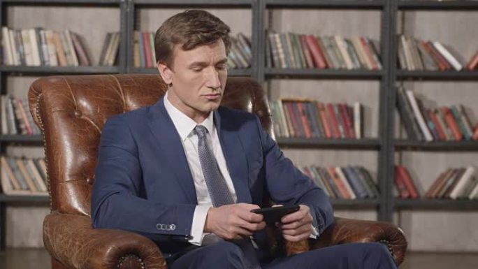 坐在椅子上的成功自信男子在手机上打字的慢动作肖像。商人在办公室使用智能手机上的应用程序微笑。商人系列