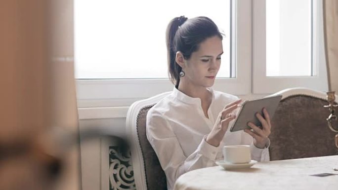 女人使用平板电脑并按桌喝咖啡