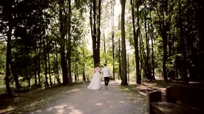 一对幸福的夫妇在婚礼当天牵着手走在公园的河岸上。漂亮的白色服装