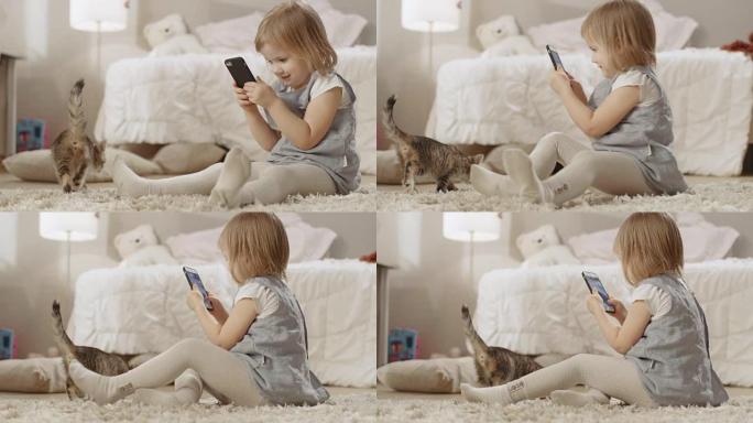 可爱的小女孩坐在地板上，用智能手机拍摄她的条纹小猫四处走动的视频。慢动作。