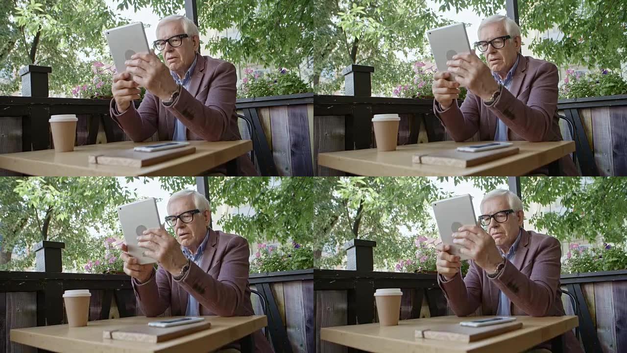 在户外咖啡馆使用数字平板电脑的高级男子