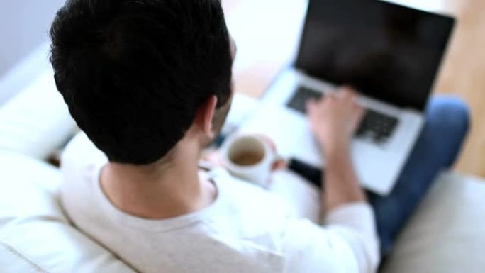 男子在使用笔记本电脑时喝白咖啡