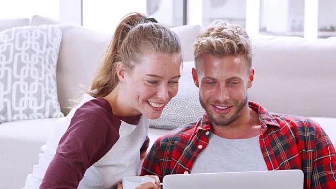 年轻的白人夫妇坐在家里的地板上使用笔记本电脑