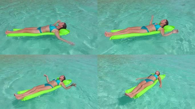 慢镜头:阳光明媚的暑假里，快乐的年轻女子躺在充气床垫上，在清澈的海水表面上漂浮