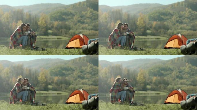 男人和女人坐在背上的毯子上，在湖边露营时喝咖啡