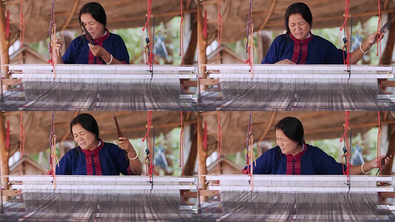 传统的泰国纺织品制造商在工艺村，老妇女在木制编织线机上工作，并纺纱制作棉织物。