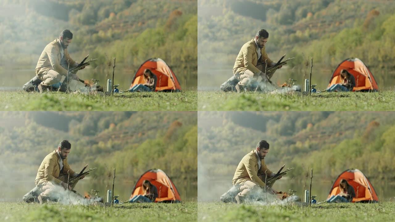 男子为篝火做准备，而女友在帐篷旁看书
