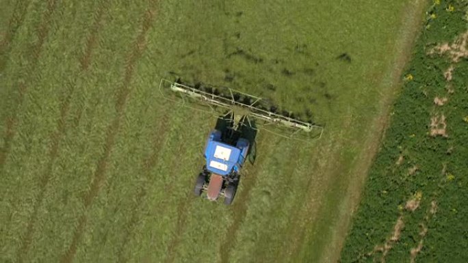 空中: 在拖拉机上飞来飞去tedding用耙子在农田上割草