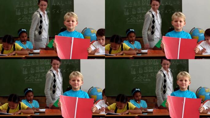 教室里拿着红色记事本的小男孩对着相机微笑