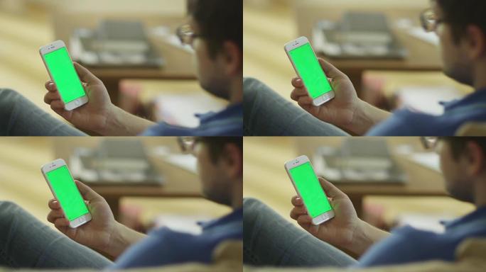 男子在家中手持带有绿色屏幕的手机，处于肖像模式