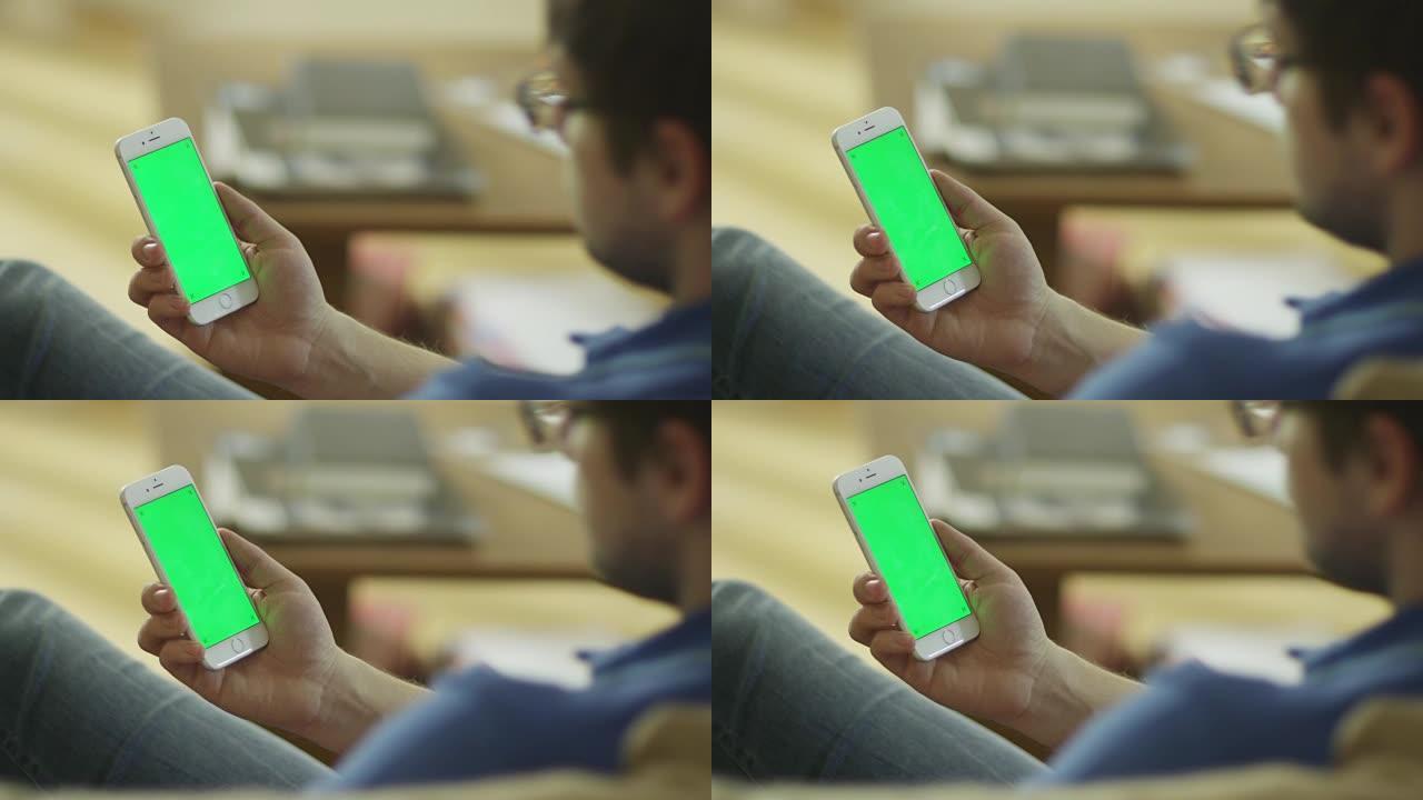 男子在家中手持带有绿色屏幕的手机，处于肖像模式