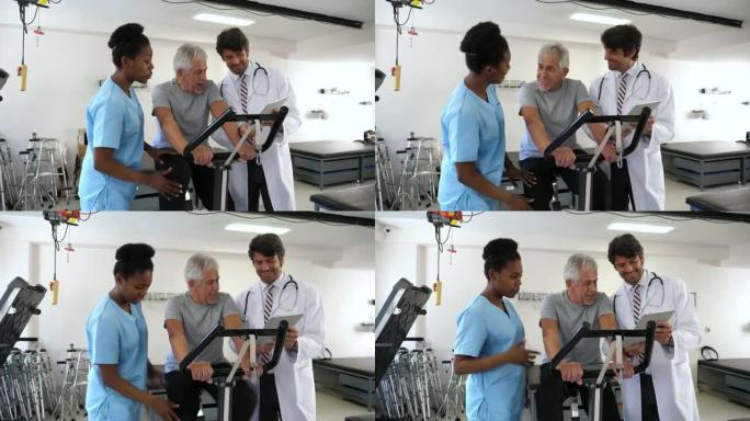 物理康复诊所的高级患者在静态自行车上锻炼，站在他旁边的骨科医生和理疗师一边看着平板电脑一边说话
