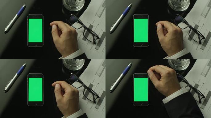 商人使用桌子上的绿屏手机。顶视图。