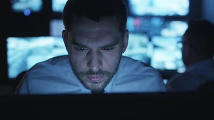 紧张而疲惫的安全人员正在充满显示屏的黑暗监控室里的计算机上工作。