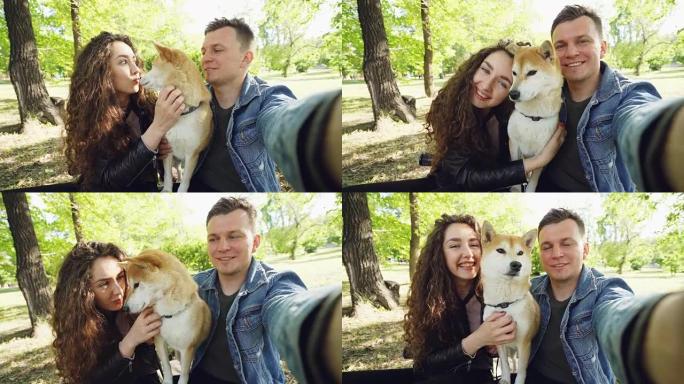 已婚夫妇与宠物shiba inu狗自拍的观点镜头，年轻人看着相机说话，笑着爱抚动物。